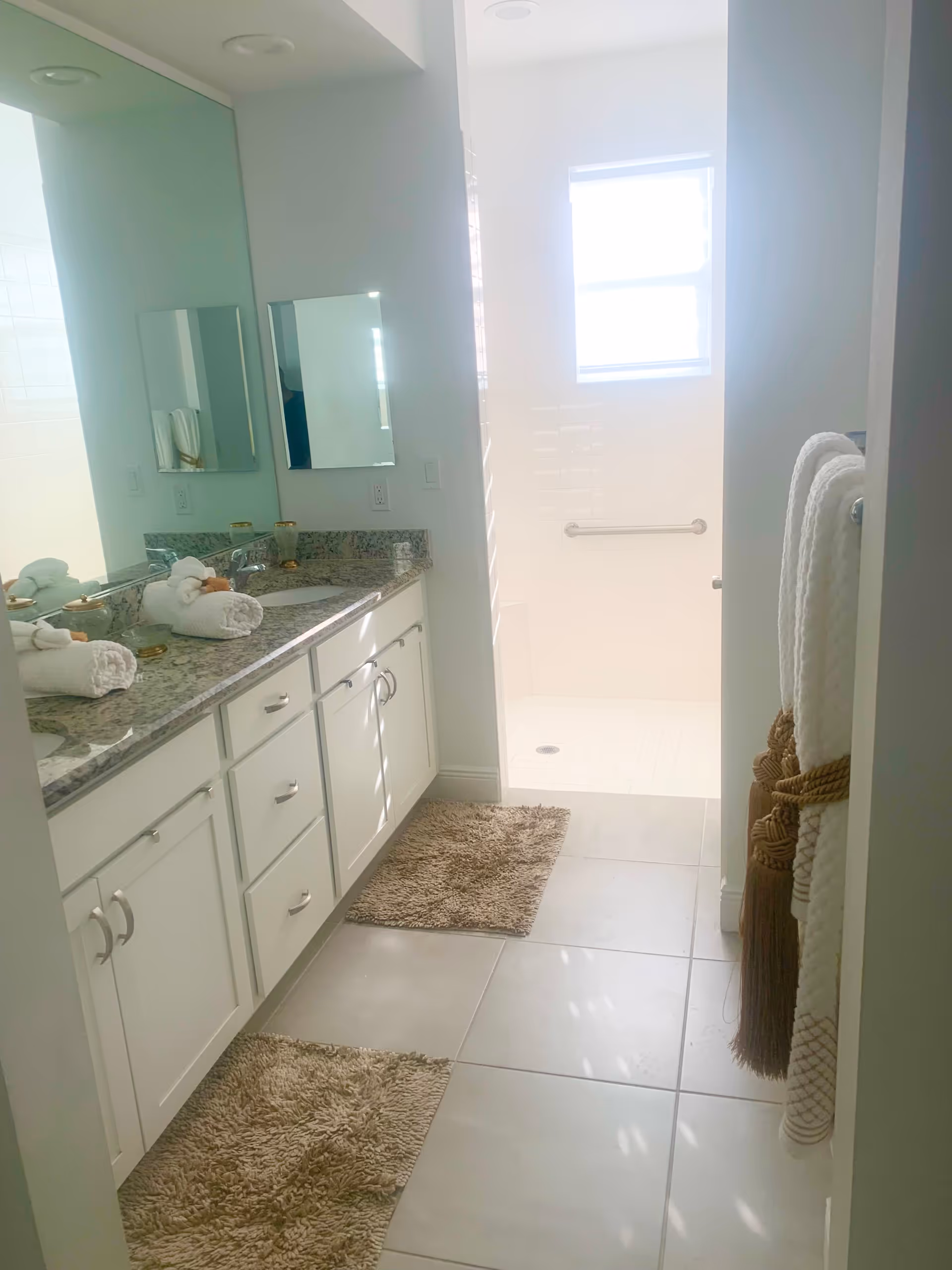 Bright bathroom featuring a double vanity, mirrors, towels, and a walk-in shower.