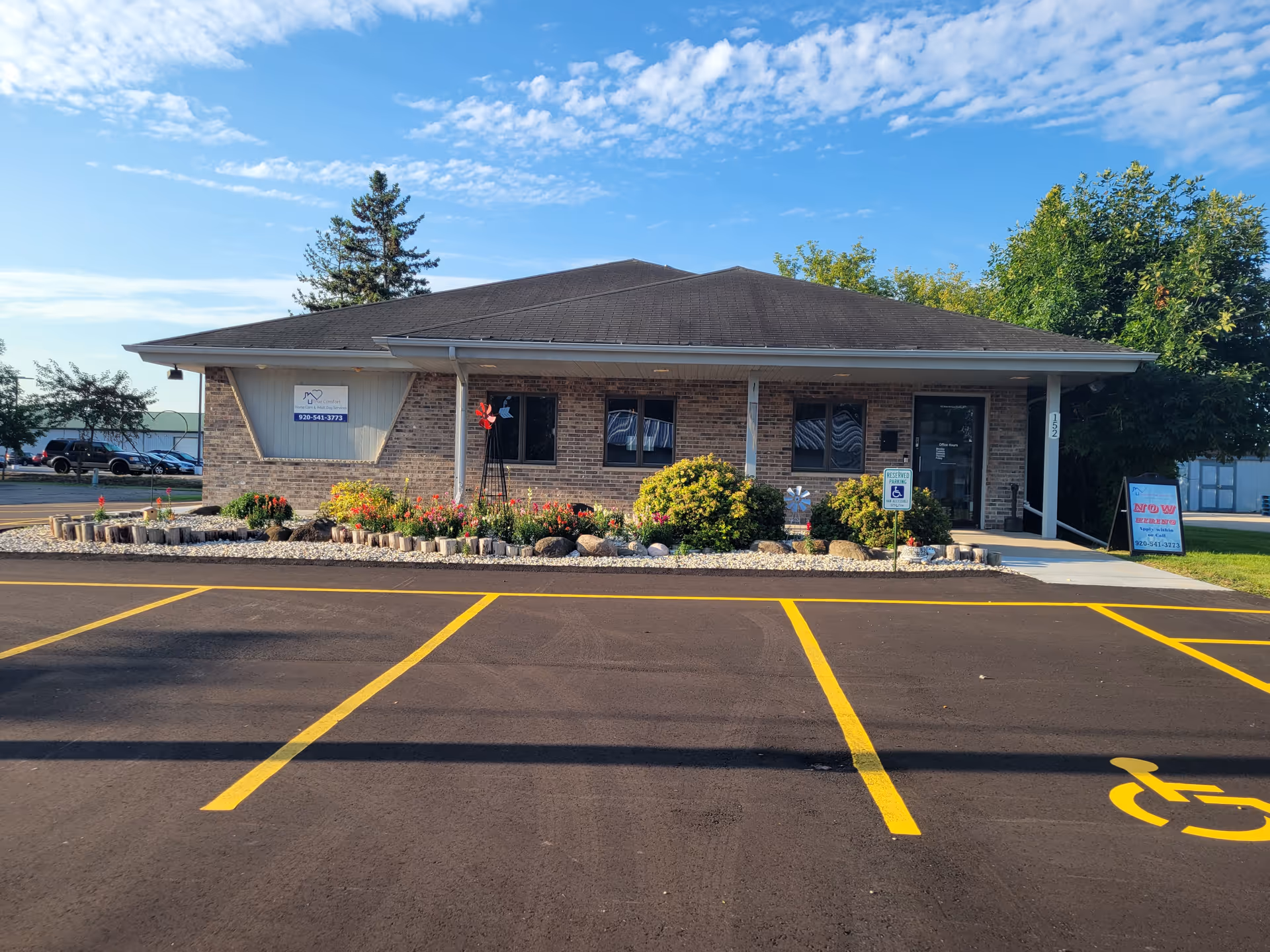 Single-story brick building with manicured front garden, parking lot, and wheelchair-accessible entrance.