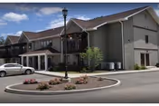 Exterior view of a senior living building with a driveway, landscaping, and a parked car.