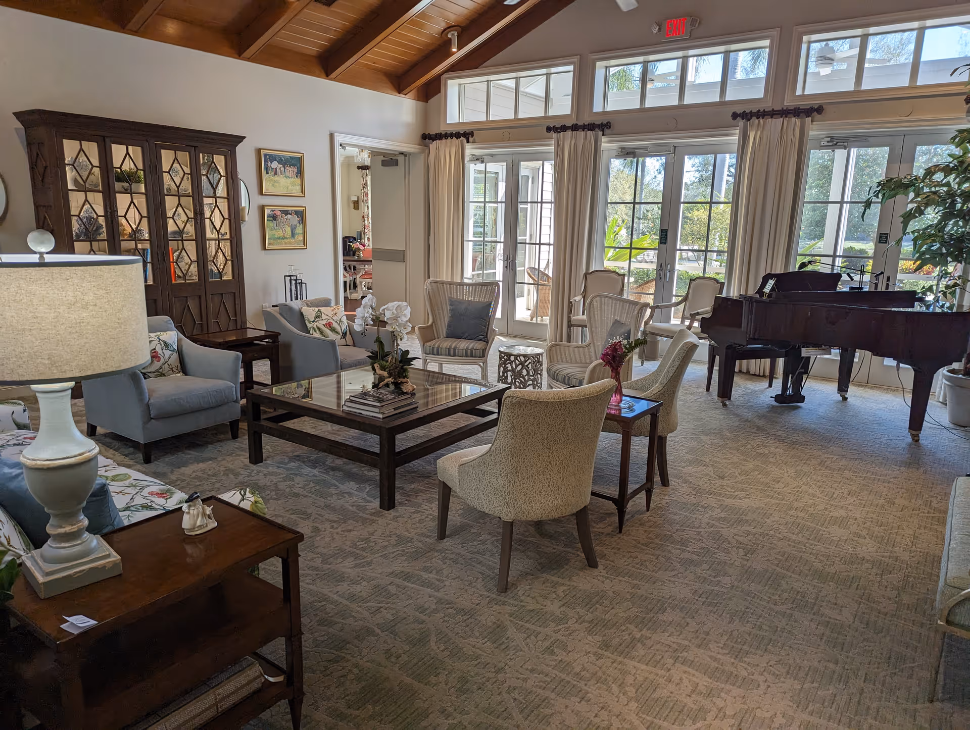 Cozy living room lounge with sofas, chairs, piano, and glass doors to the outdoor patio.