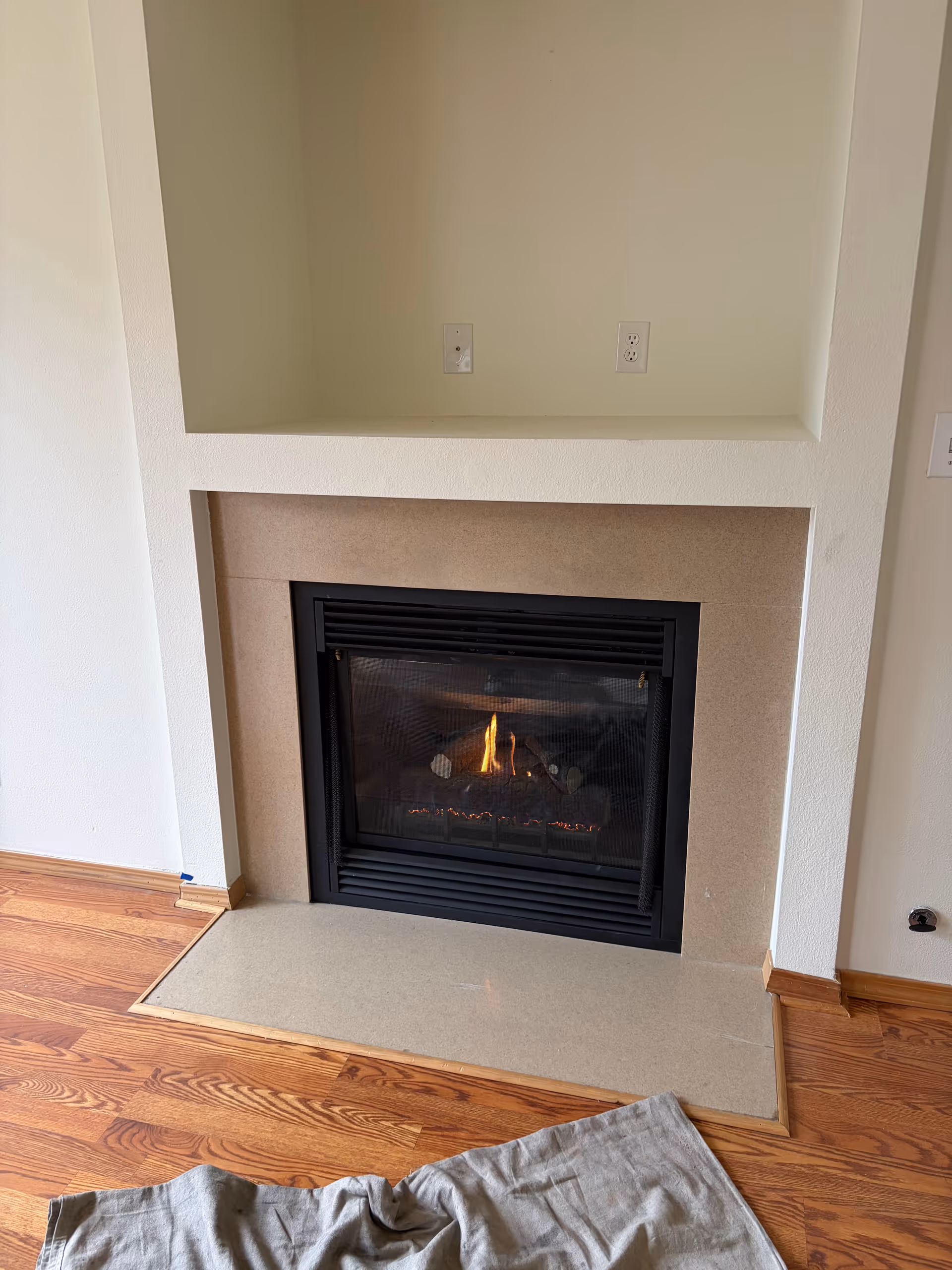 Interior living area with a gas fireplace in a beige surround and wood flooring.