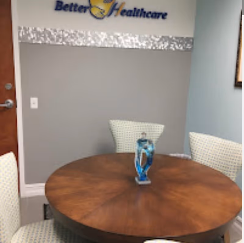 Round wooden table with white chairs in a small Better HealthCare conference room.