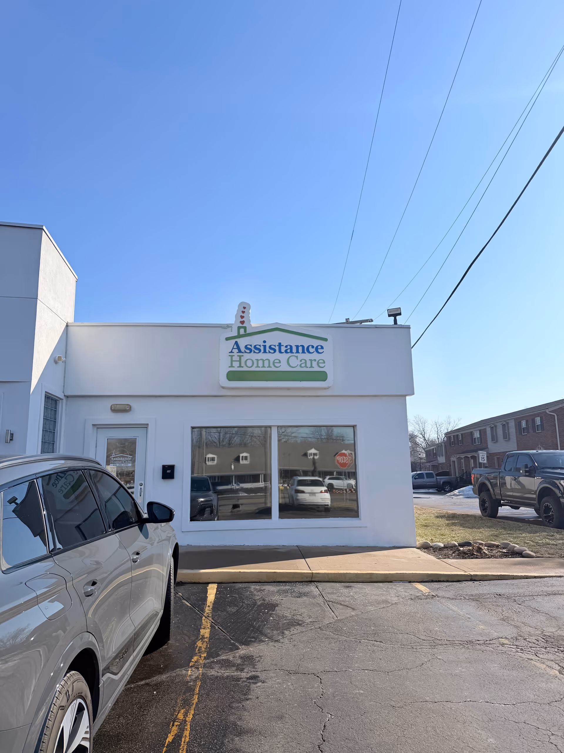White storefront building with Assistance Home Care sign, parked cars, clear blue sky