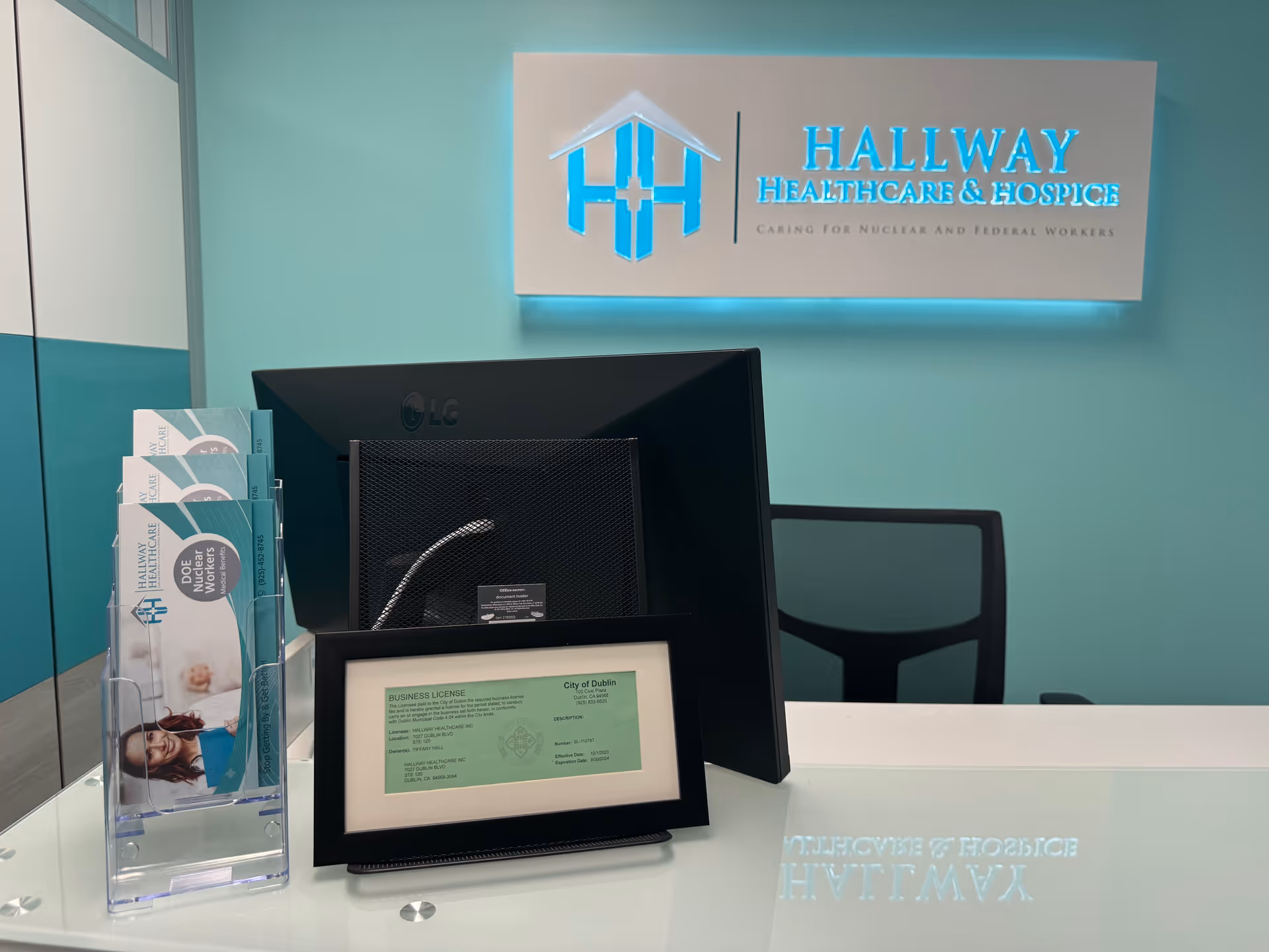 Reception area inside teal-walled building with sign, monitor, and brochure stand.