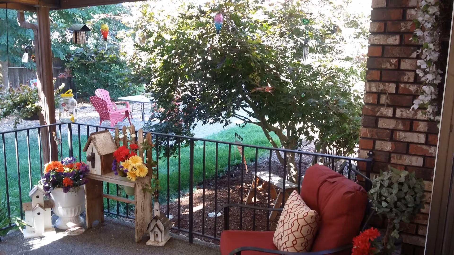 Outdoor porch area with red cushioned chair, garden decor, and colorful chairs for relaxing outdoors.