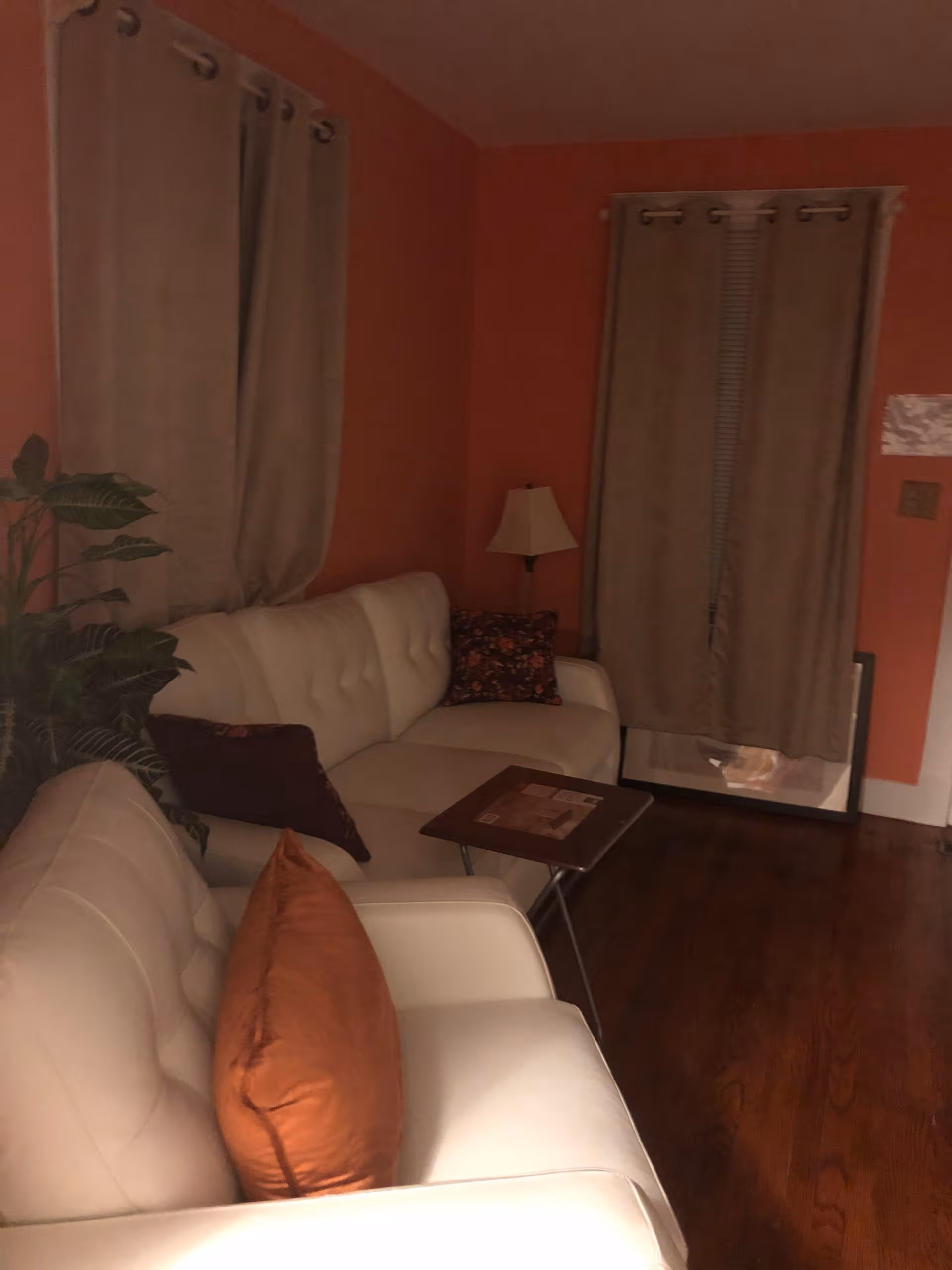 Cozy living room with white leather sofas, a small table, lamp, and plant.