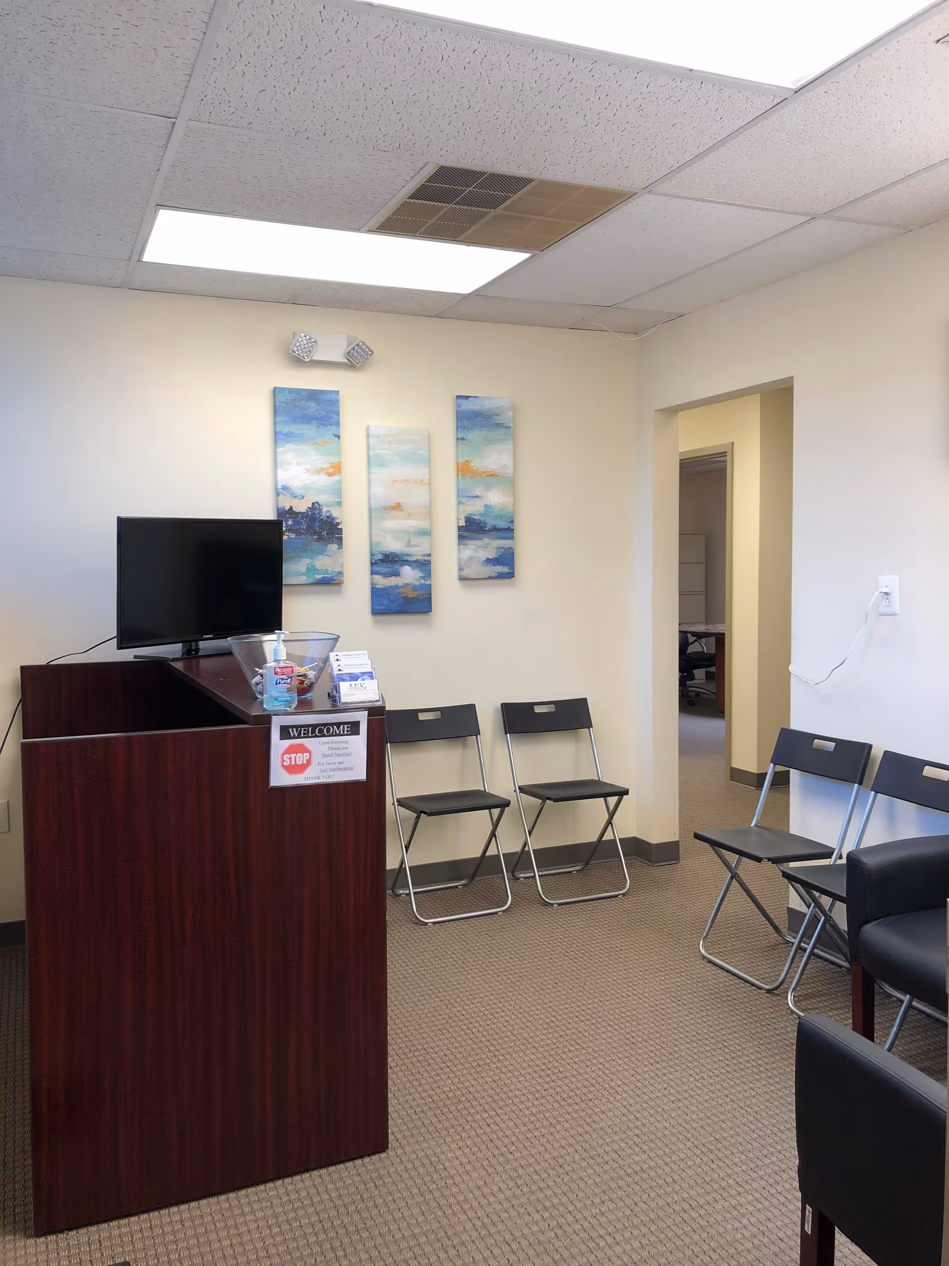 Interior reception area with podium, TV, wall art, and folding chairs.