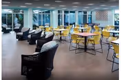 Bright dining area with yellow chairs around round tables and wicker lounge chairs.