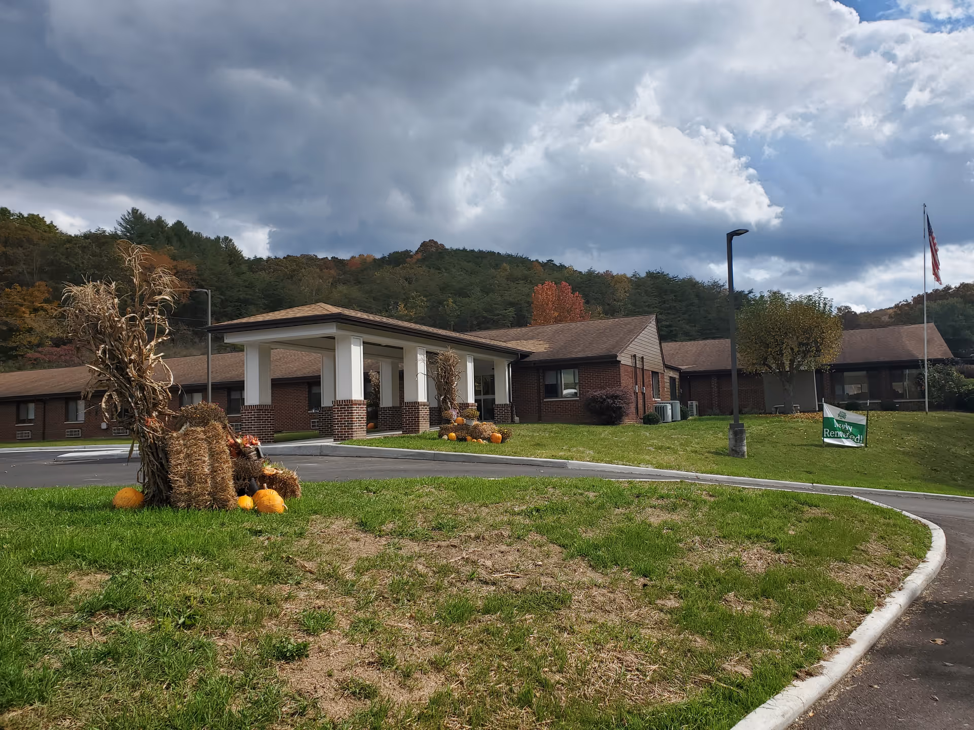 Exterior view of a single-story brick senior care center with a curved driveway and autumn decorations.