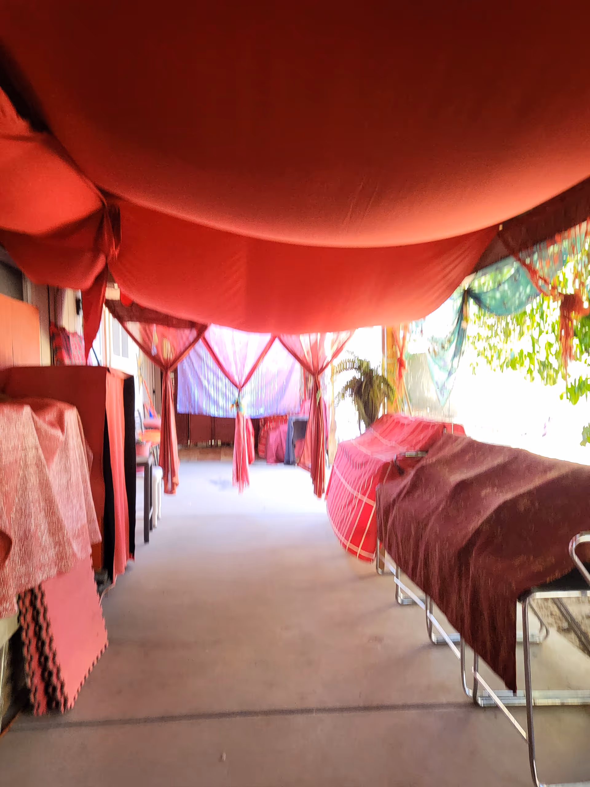 Narrow interior hallway with multiple beds covered in red sheets under draped fabric