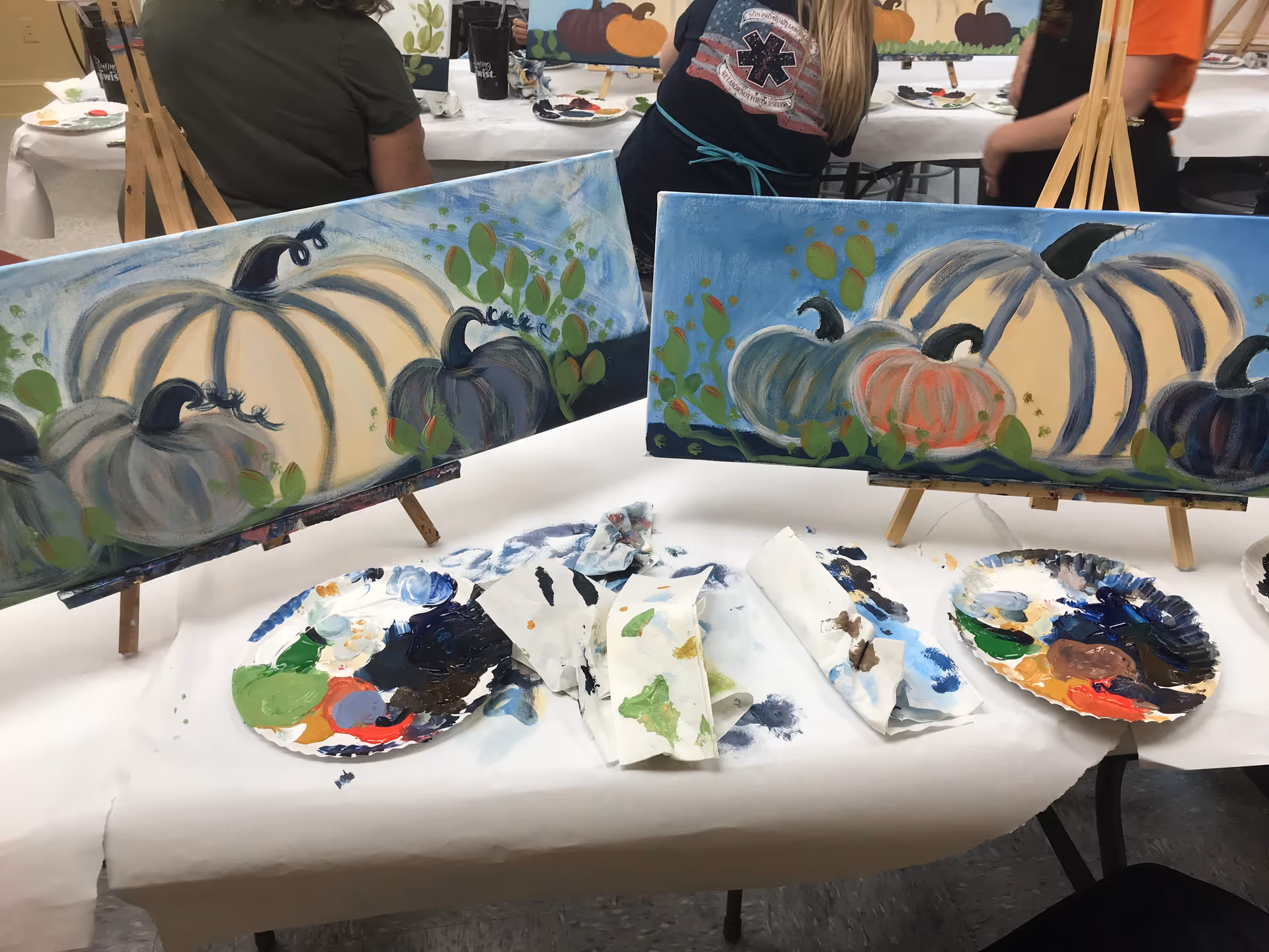Indoor art activity with pumpkins painted on canvases and painting supplies on a table.