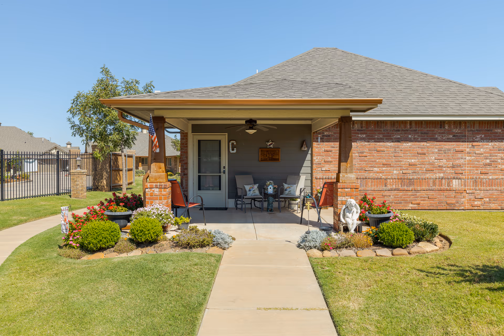 Front entrance and covered porch of a single-story brick residence with seating, potted plants, and a walkway.