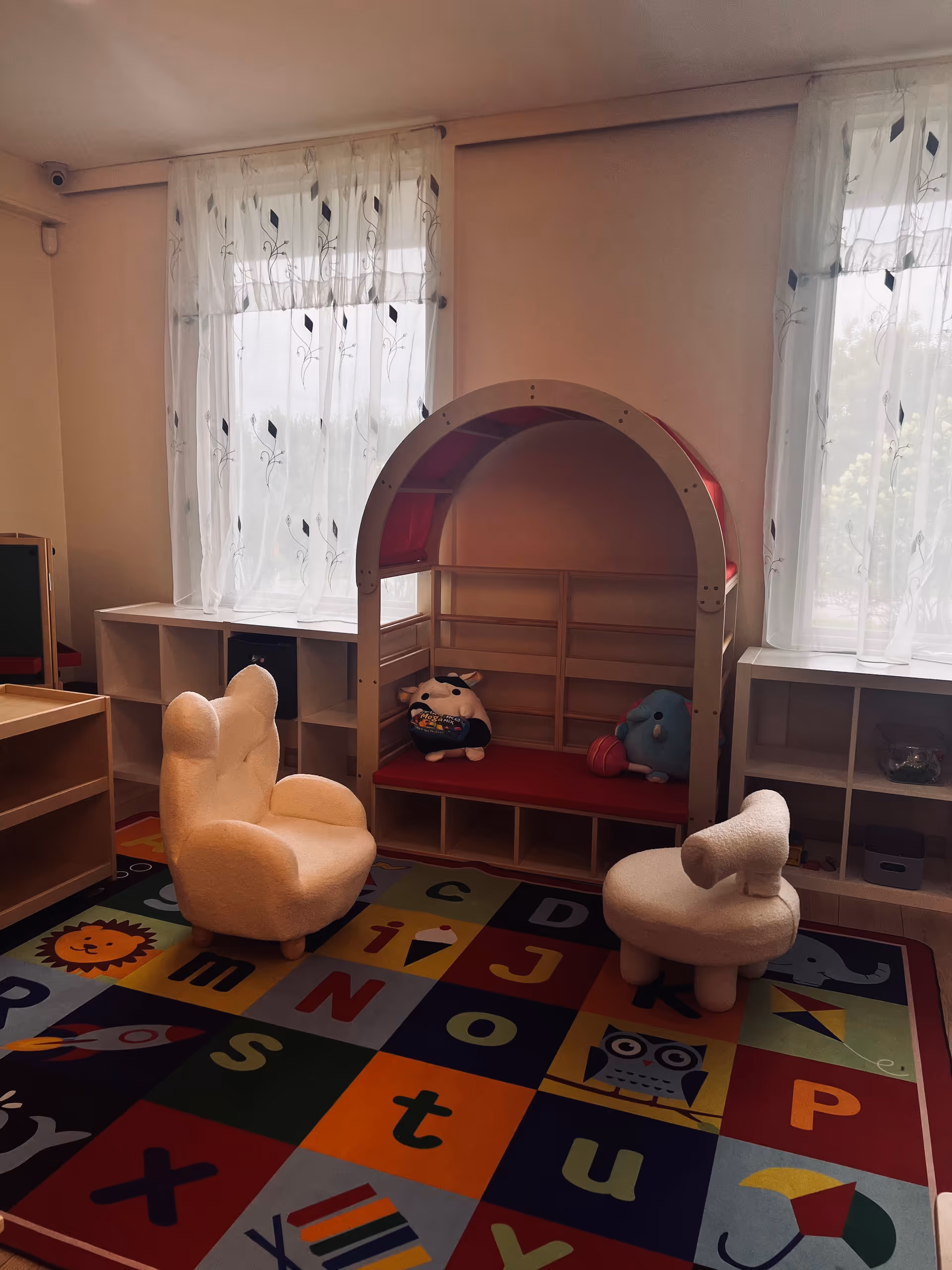Bright indoor play area with a colorful alphabet rug, small furniture, and a toy house.