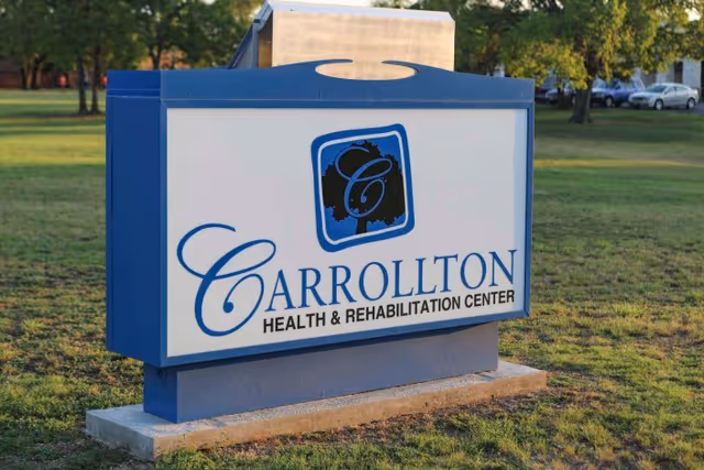 Freestanding blue-and-white sign that reads 'Carrollton Health & Rehabilitation Center' on a grassy lawn.