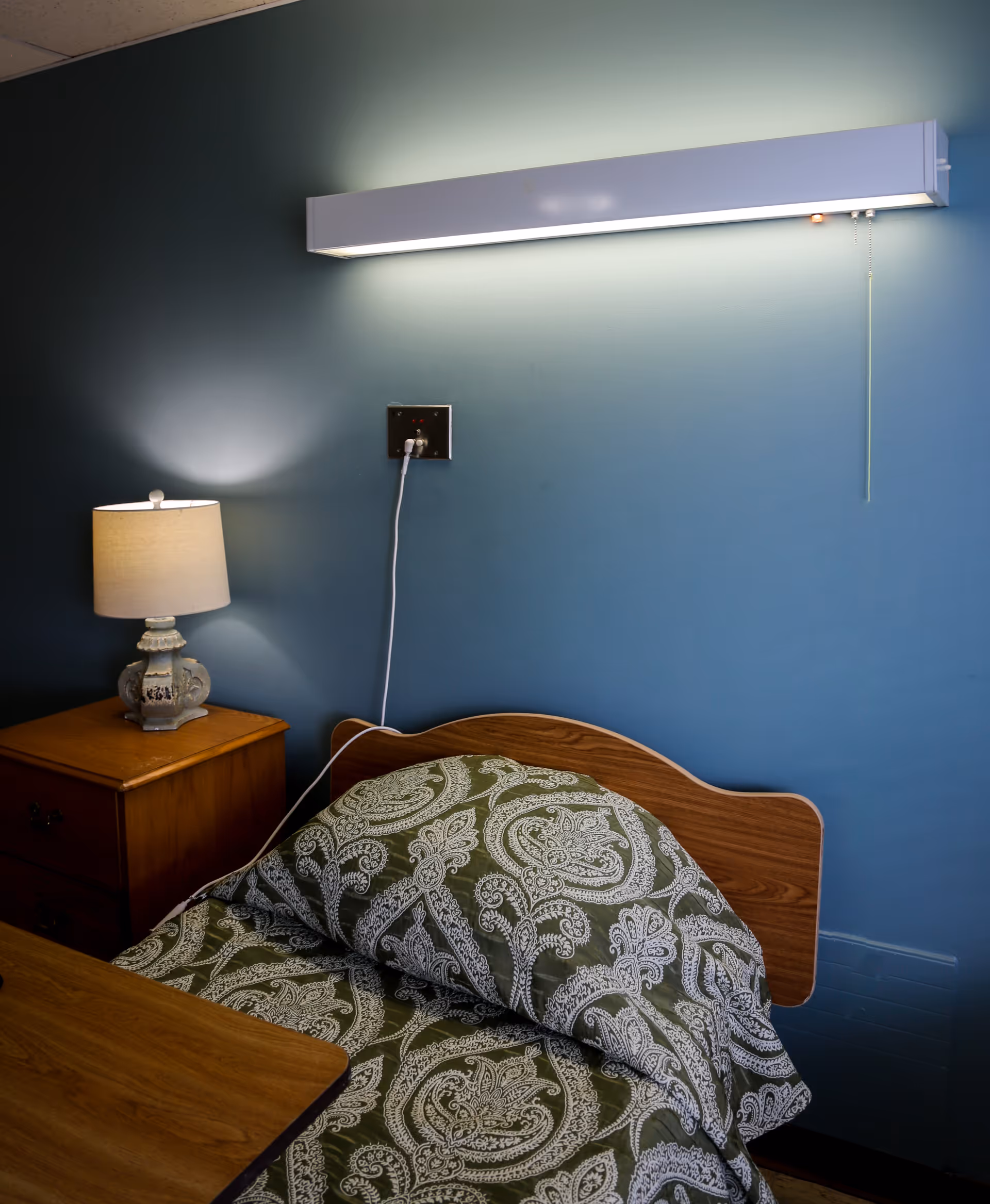 Teal-walled bedroom with a wooden bed, nightstand, and a lit lamp.