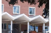 Brick senior living facility exterior with three white peaked canopies over the entrance.