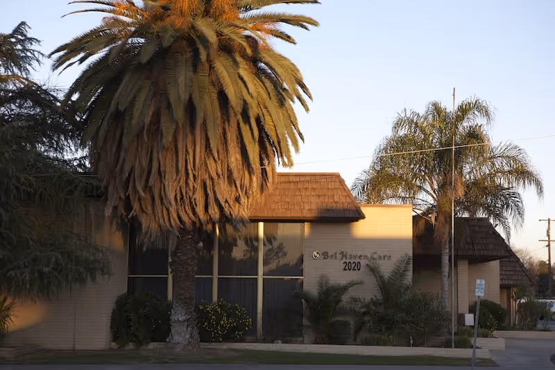 Front exterior of a senior living building with palm trees and a sign.