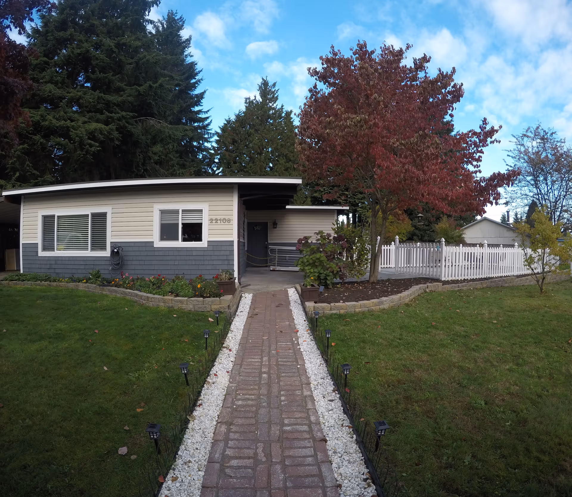 Front view of a single-story beige house with a brick walkway and white fence.