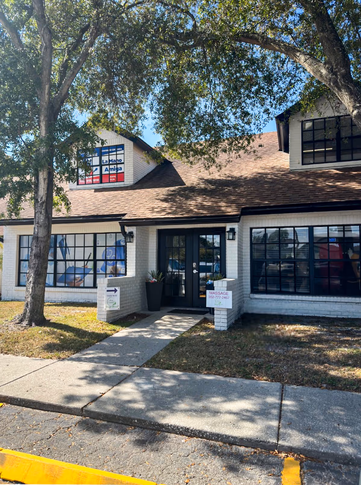 White brick senior living building front with black-framed windows and La Mano Amiga sign