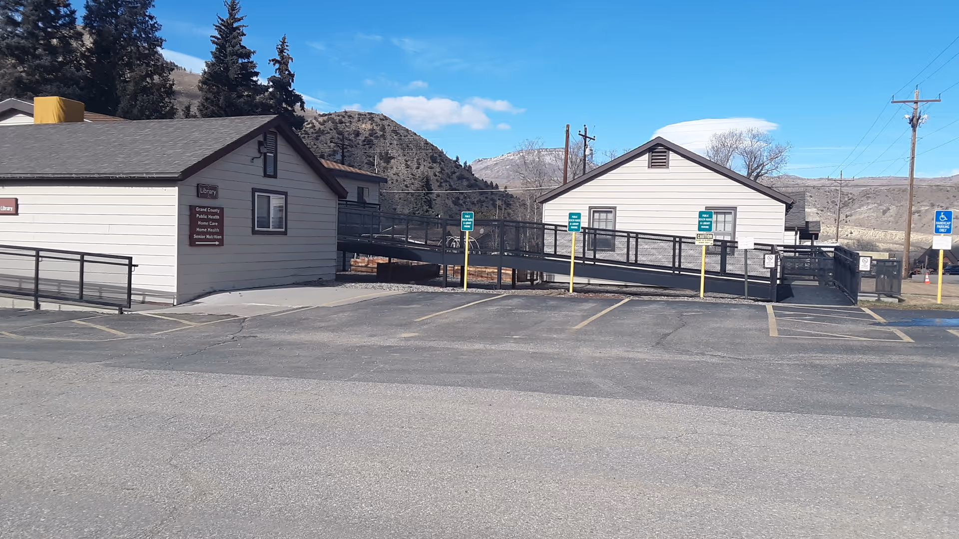 Two small beige buildings connected by a ramp, with mountains and a parking lot in foreground.