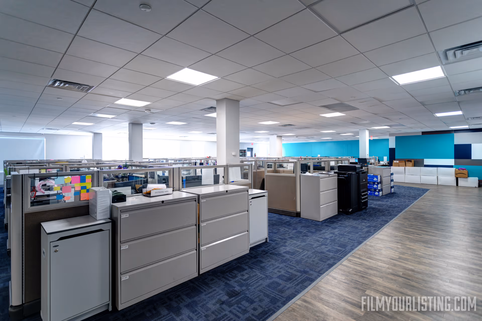 Wide open office-like workspace with cubicles, filing cabinets, and blue-accent walls.