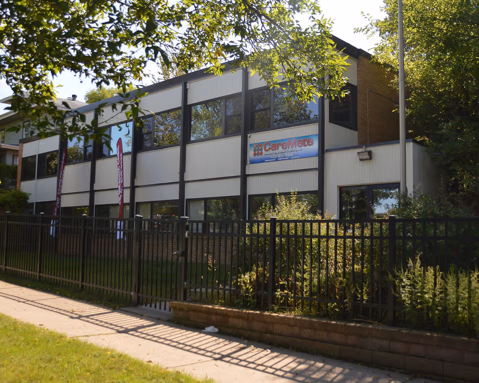 Two-story beige building with a CareMate sign, surrounded by a black metal fence.