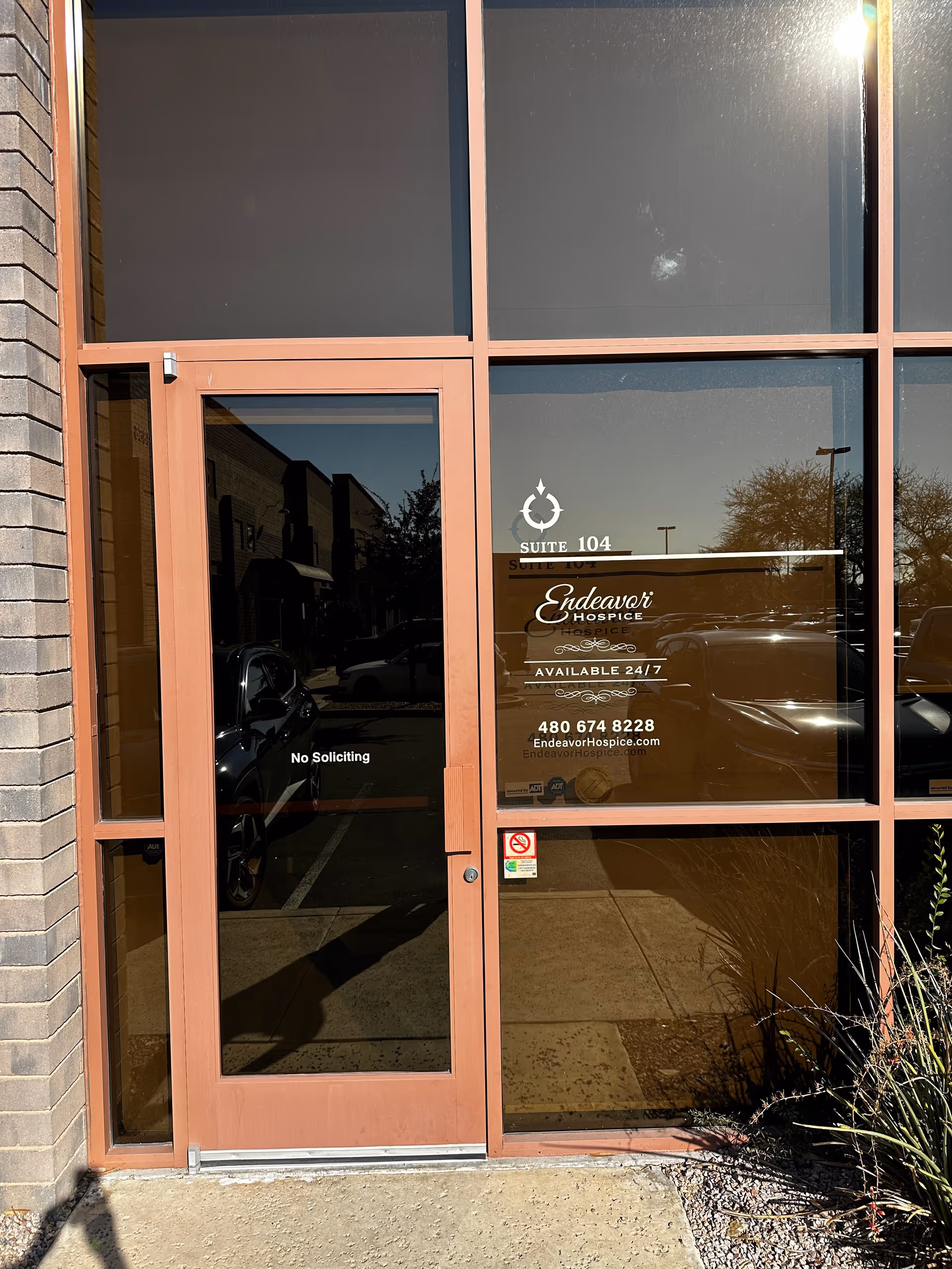 Glass entrance door of Endeavor Hospice building with suite numbers and reflections.