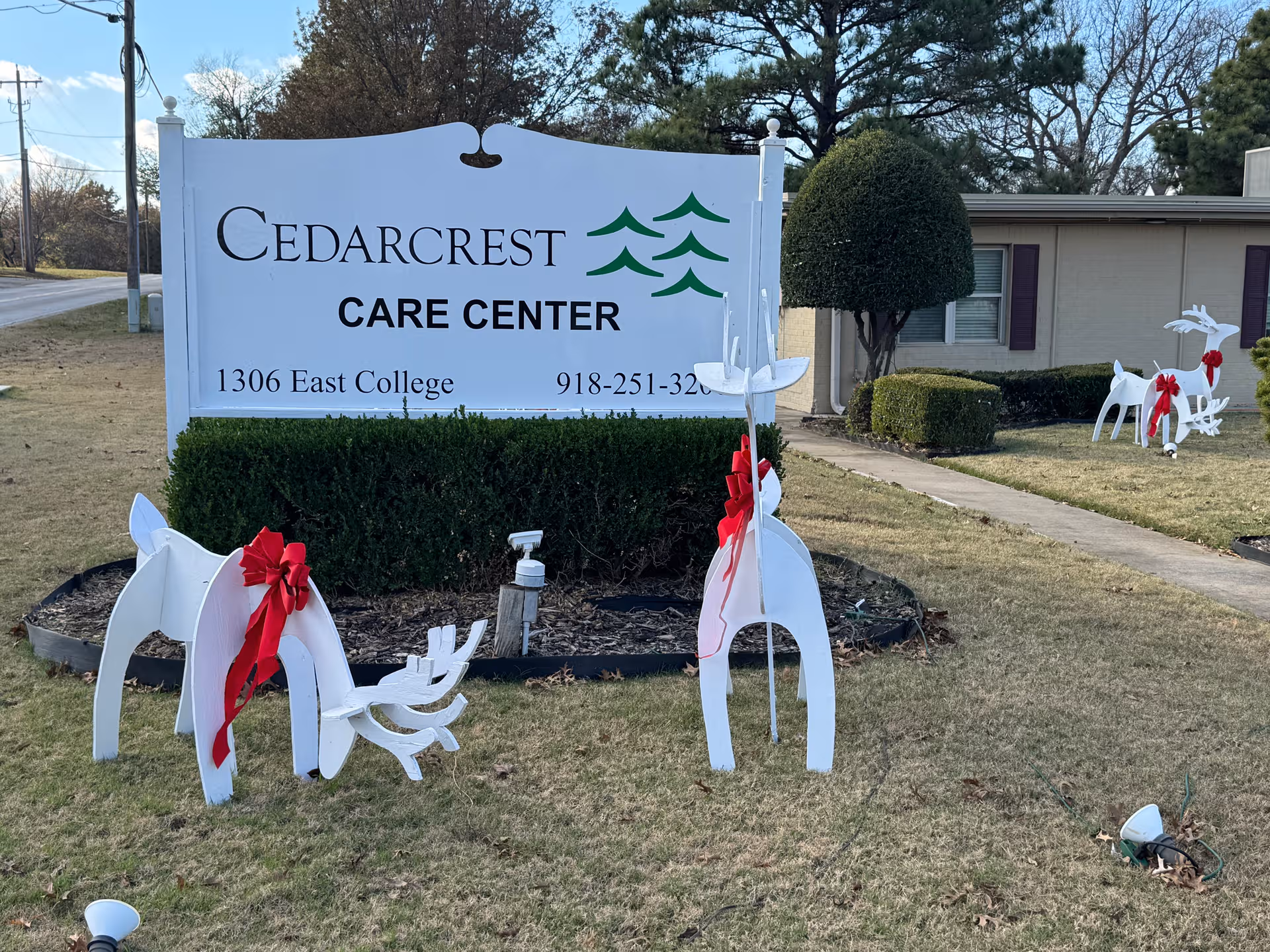 Cedarcrest Care Center sign on a lawn with white holiday sculptures and red ribbons.
