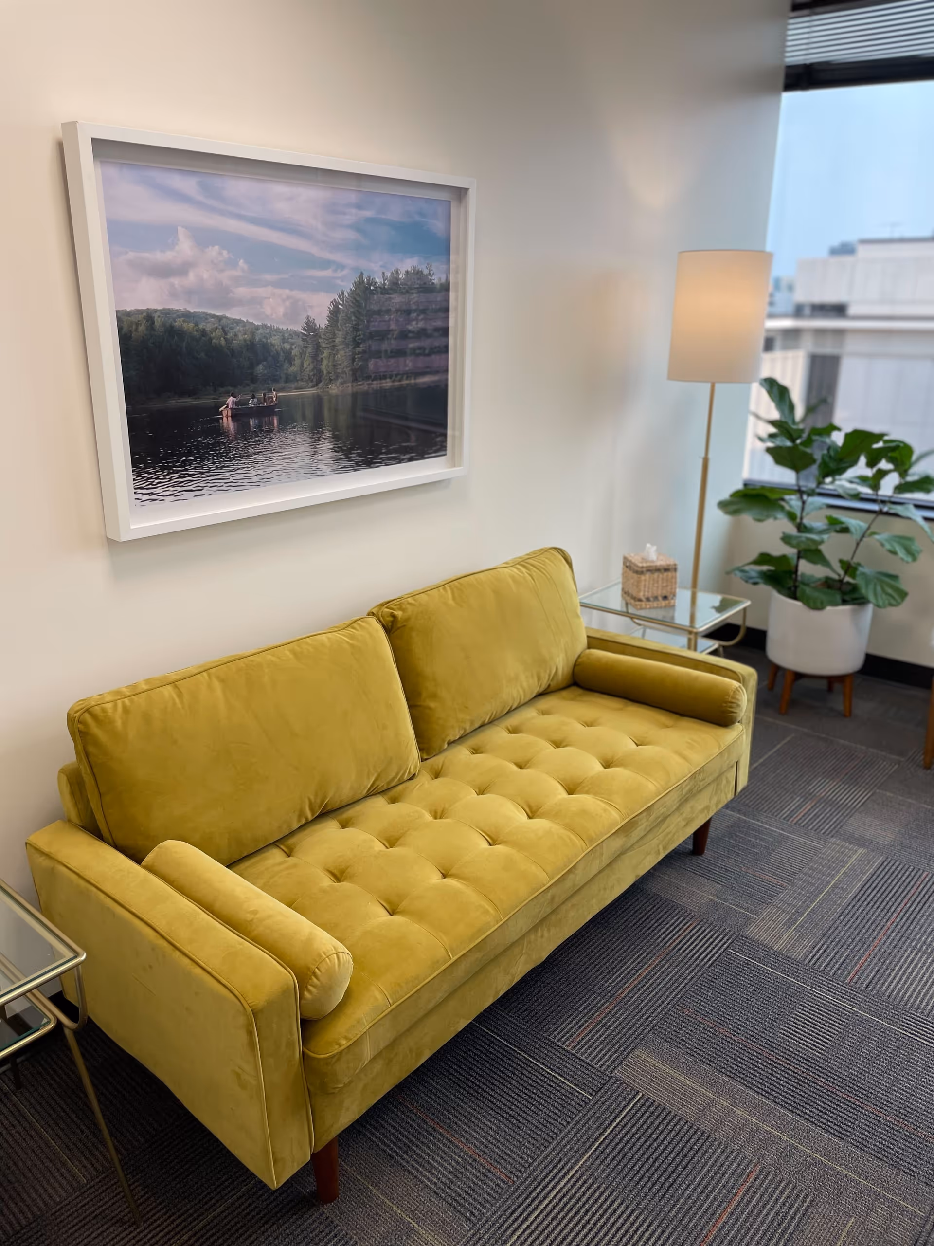 A yellow tufted sofa in a modern lounge area with a framed landscape photo.