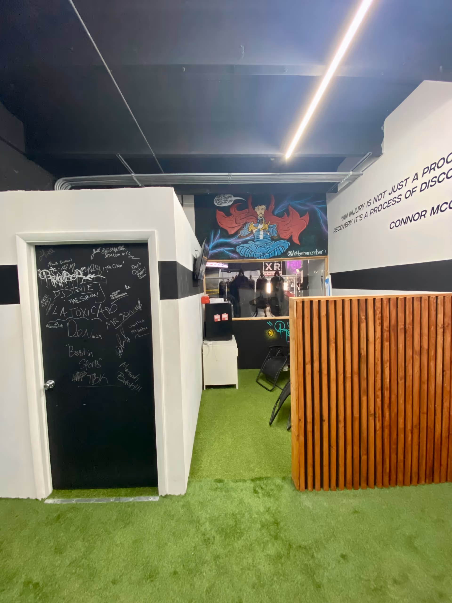 Interior hallway with chalkboard door, green turf floor, wooden divider, and mural at back.