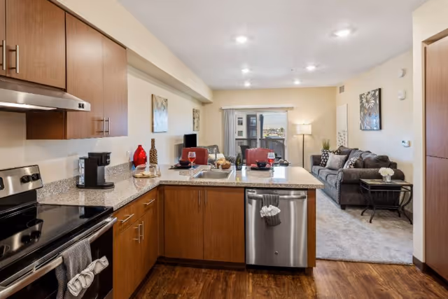 Open-concept kitchen with island overlooks a living area in a senior apartment.
