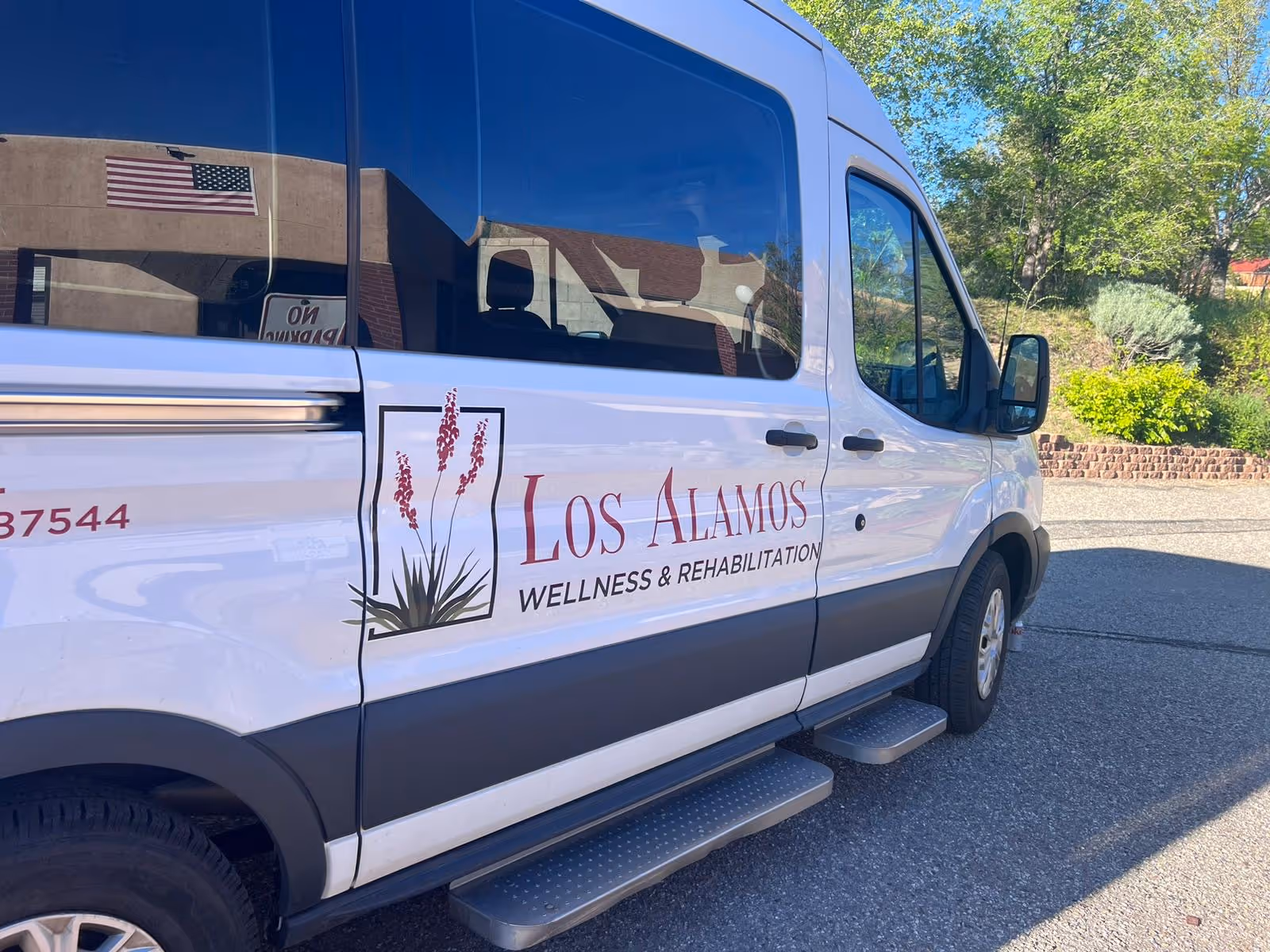 White van with Los Alamos Wellness & Rehabilitation logo parked on a sunny street.