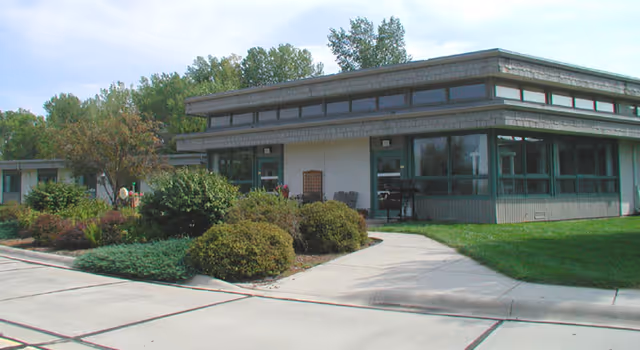 Single-story care center building with large windows, a walkway and landscaped shrubs in front.