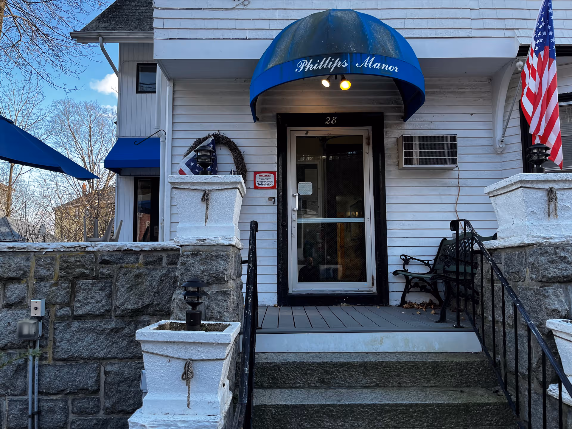 Exterior view of Phillips Manor Nursing Home entrance with blue awning and American flag.