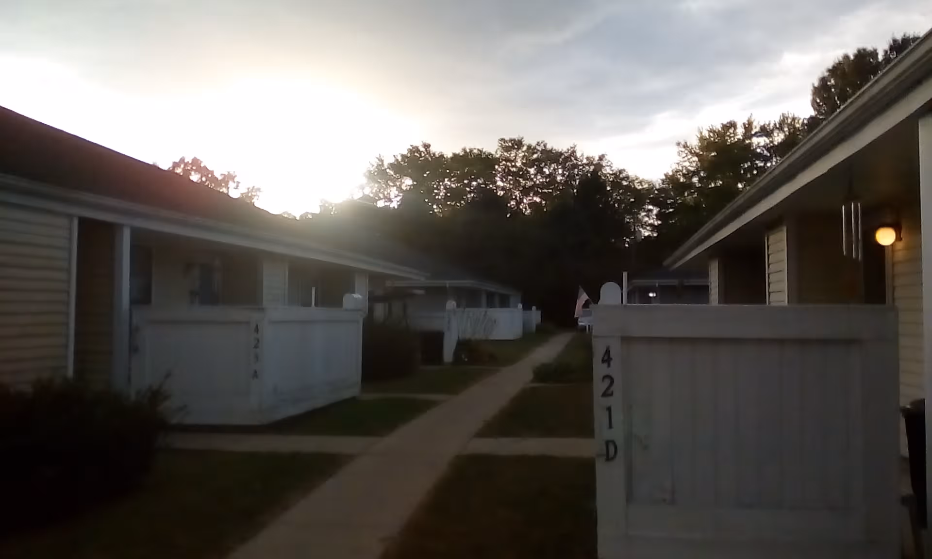 Pathway between single-story senior living units with white fences at dusk.