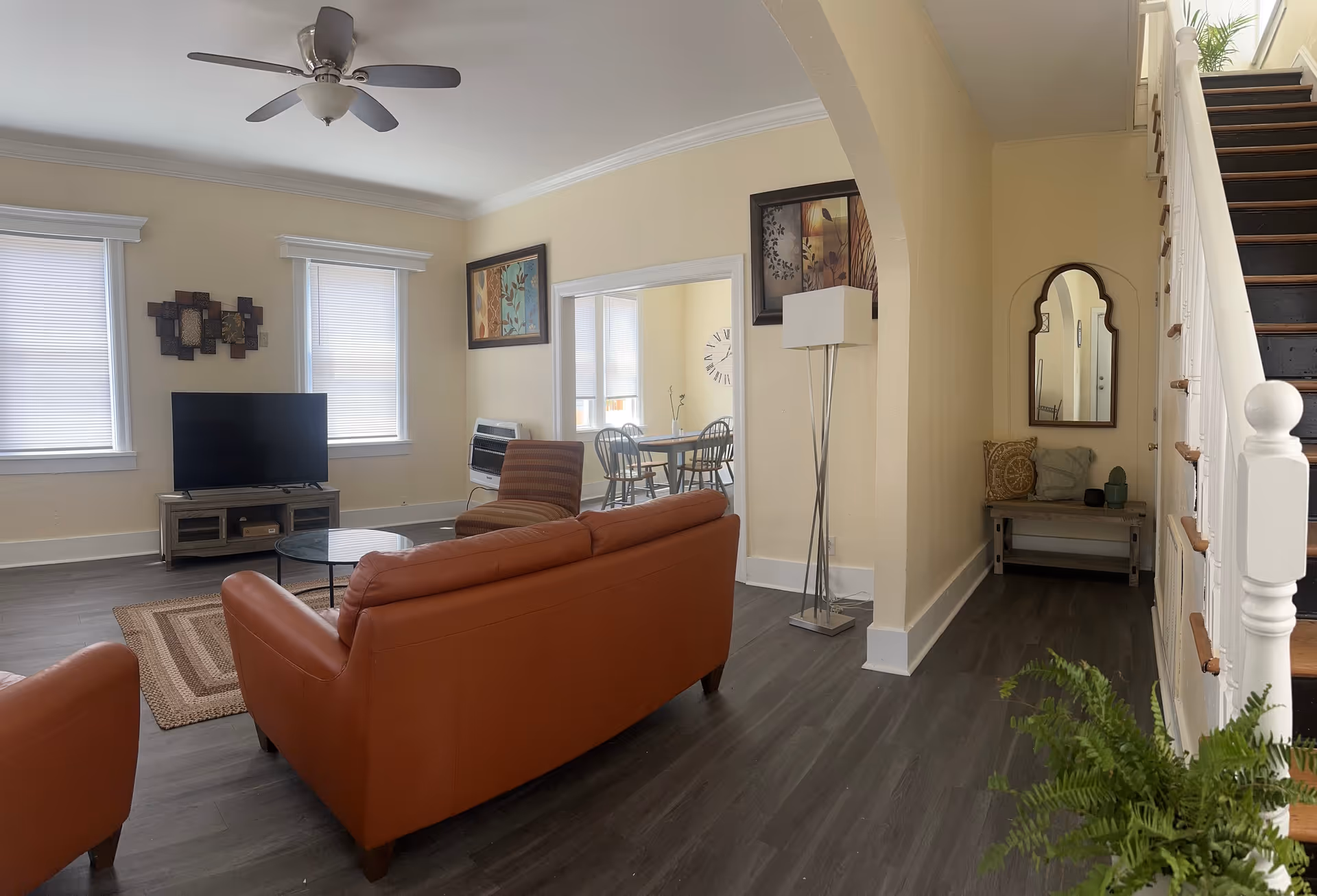 Spacious living room with brown leather sofas, TV stand, dining nook, and staircase.