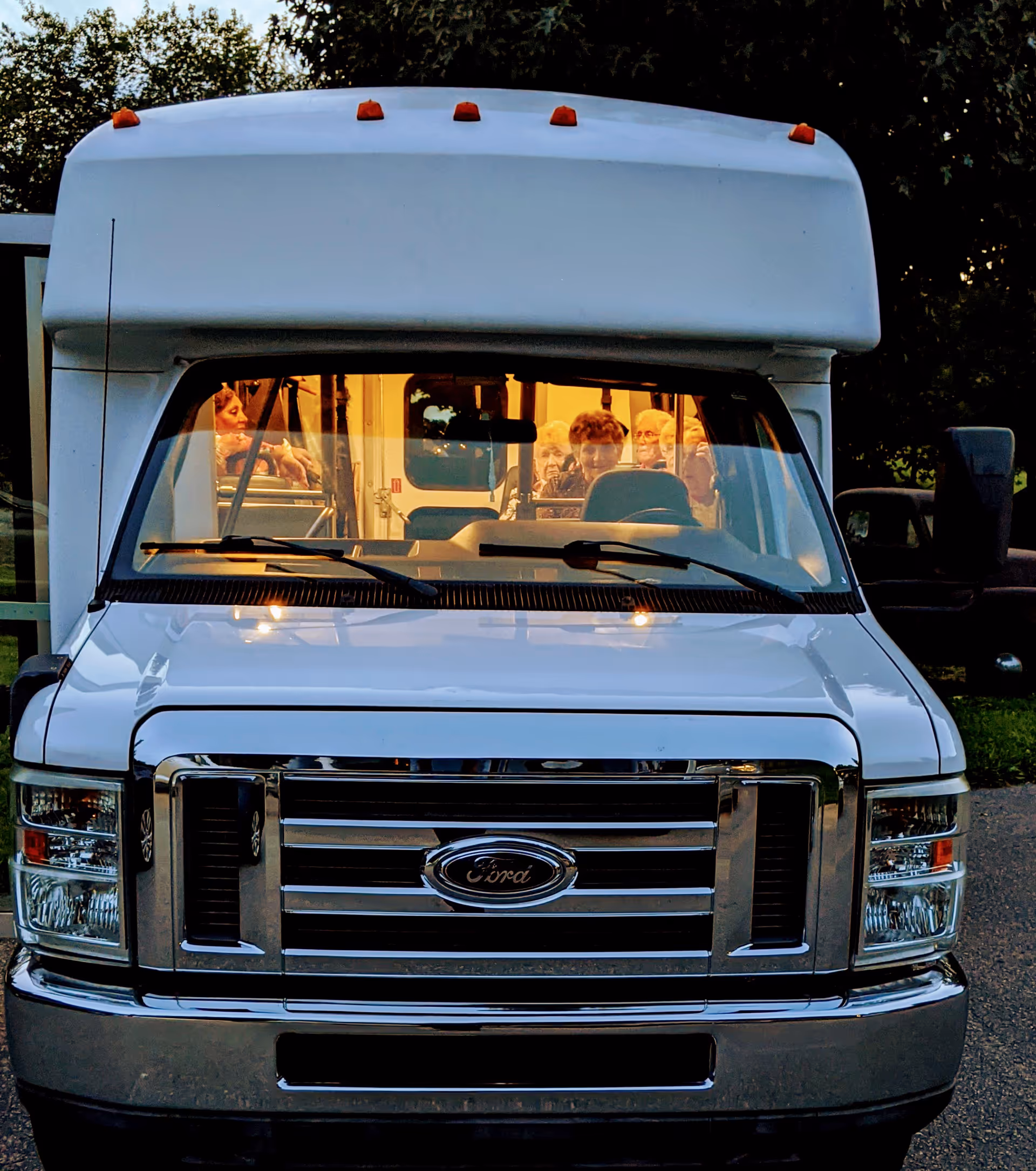 Front view of a white shuttle bus with passengers visible through the windshield.