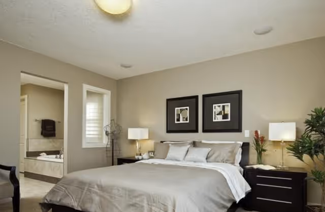 A neatly made bedroom featuring a large bed, two nightstands, lamps, and wall art.
