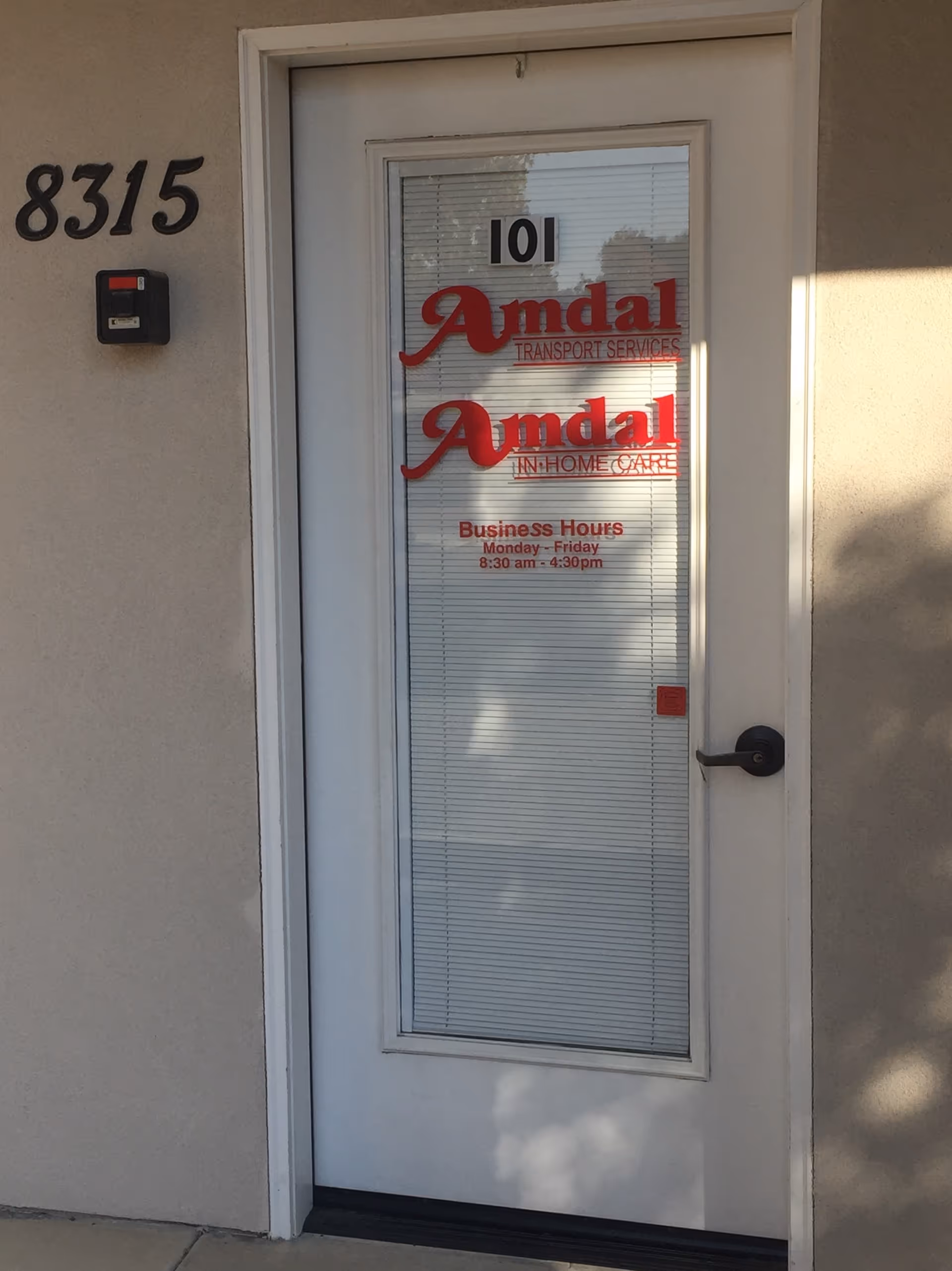 Exterior door with blinds and red Amdal logos showing In-Home Care hours.