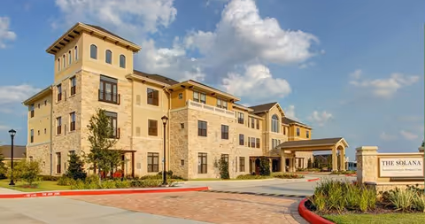 Three-story stone-clad senior living building with a porte-cochère and landscaped entrance.
