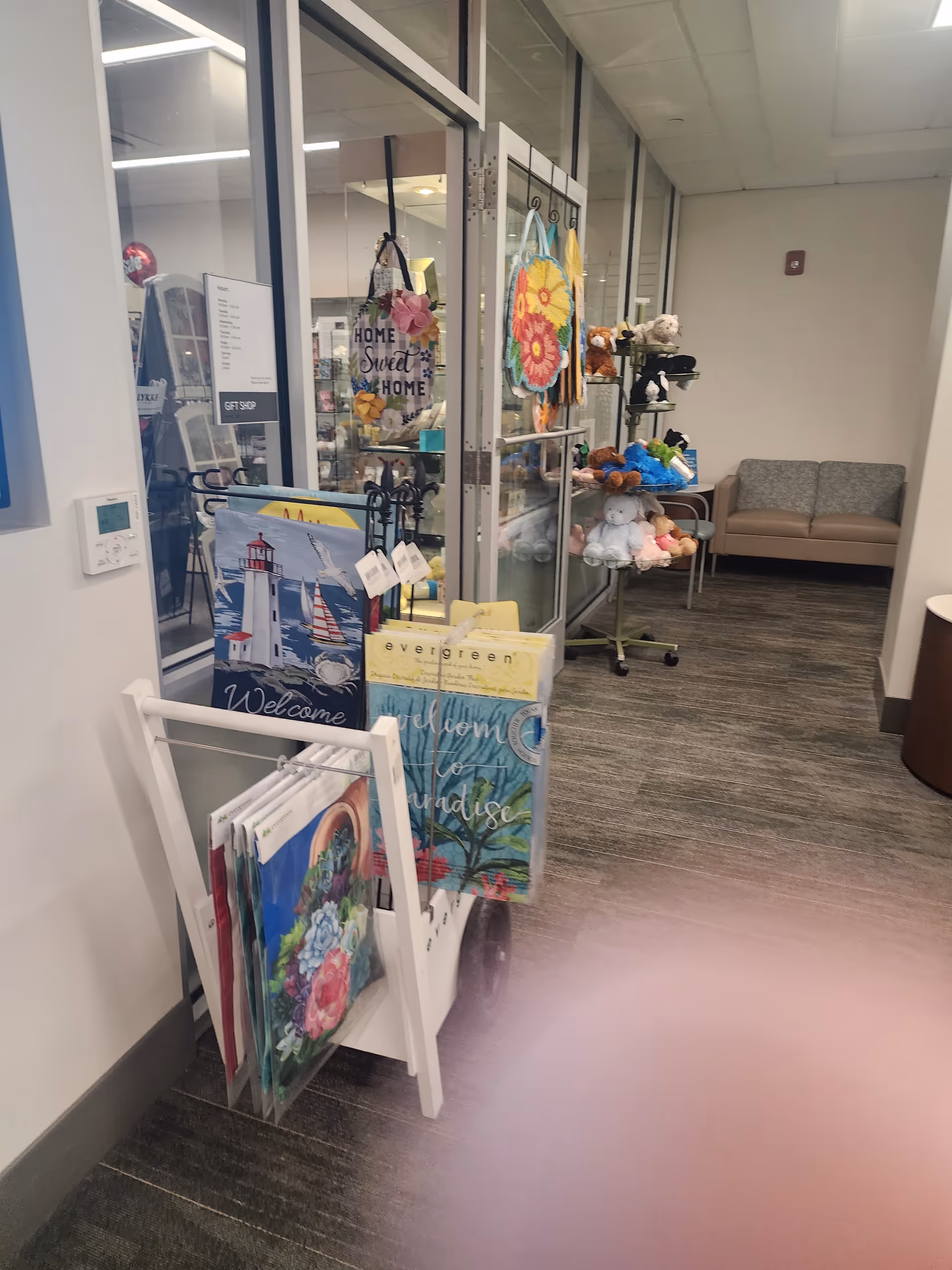 Hospital gift shop area with glass doors, greeting cards, stuffed toys, and a beige couch.