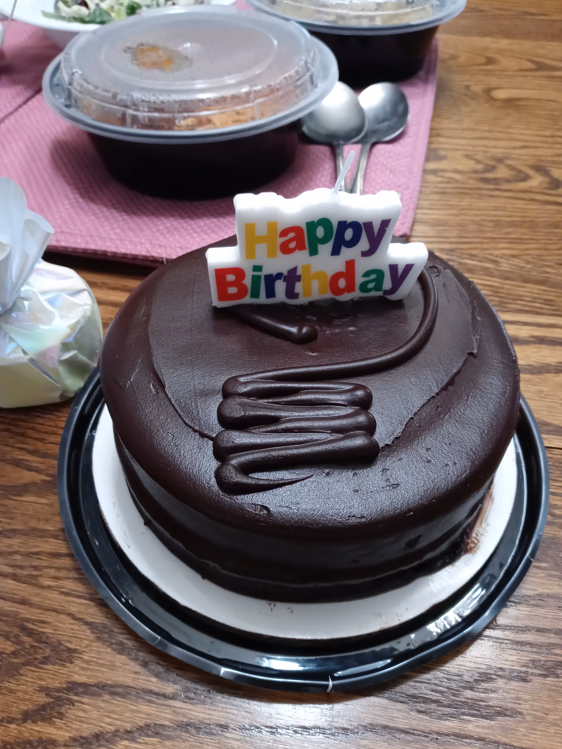 A chocolate birthday cake with a colorful 'Happy Birthday' topper on a table.