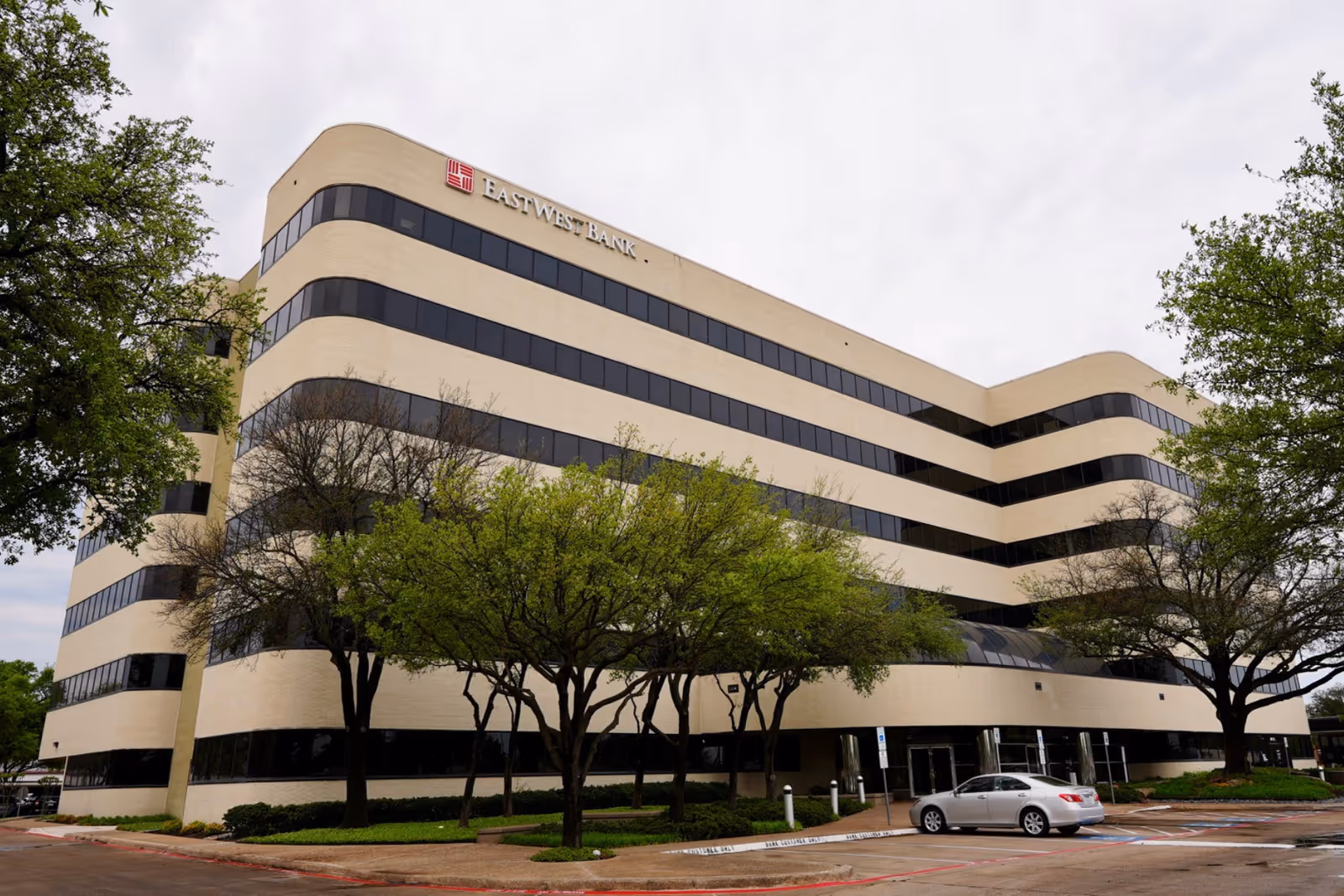 Large curved beige office building with dark windows and surrounding trees.