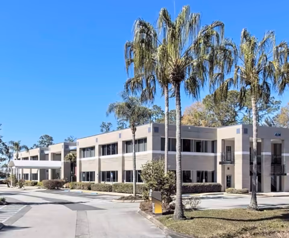 Two-story senior housing building with palm trees and a driveway in sunny setting