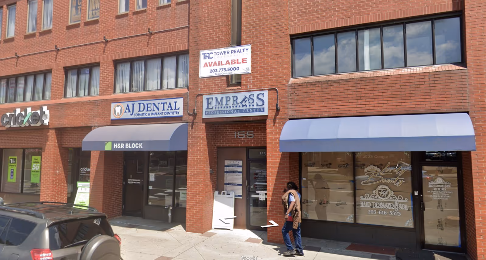 Brick storefront building with signage and a pedestrian walking on the sidewalk.