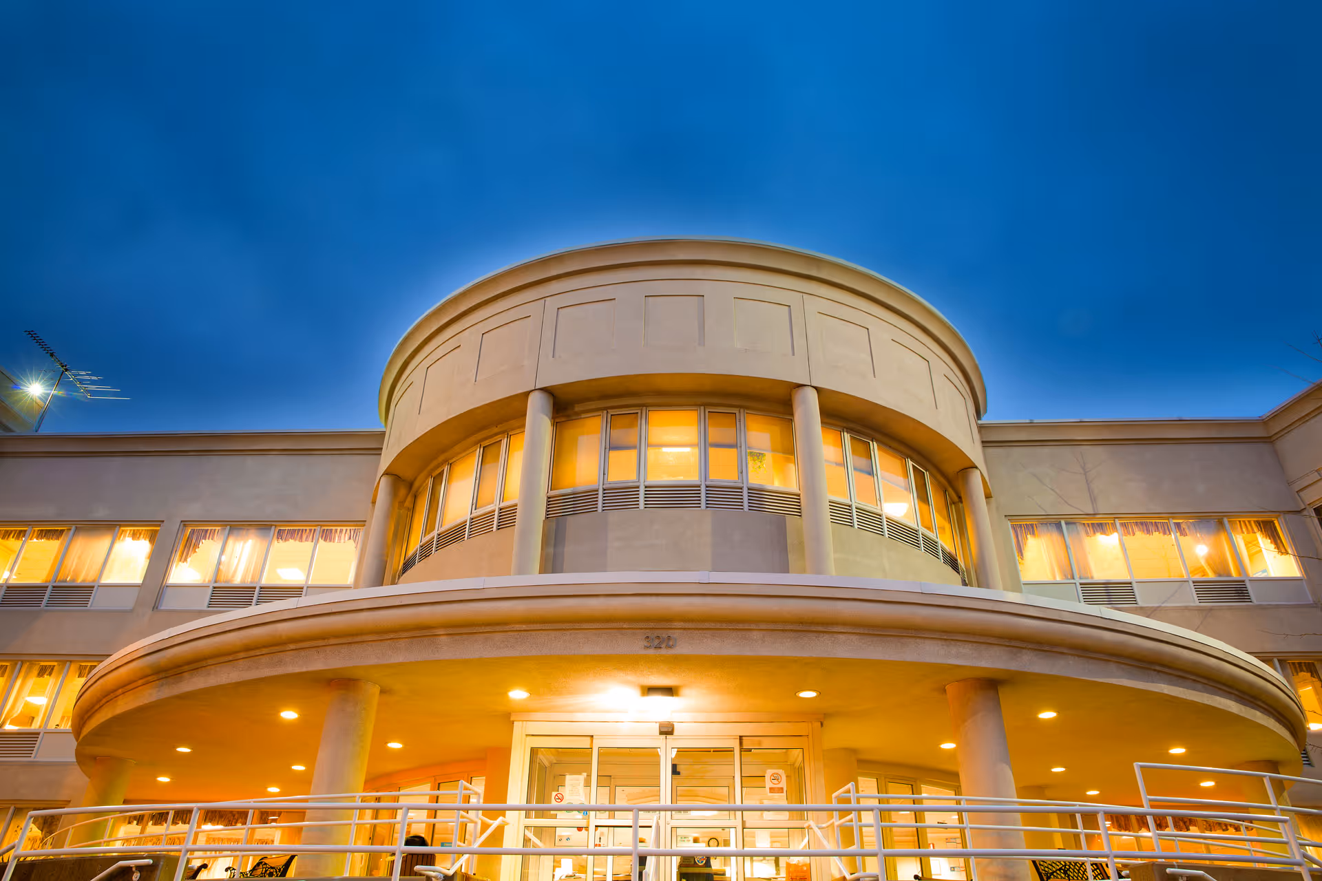 Exterior front view of Meadowbrook Care Center - Freeport building at dusk, showing a rounded entrance with columns and illuminated windows.