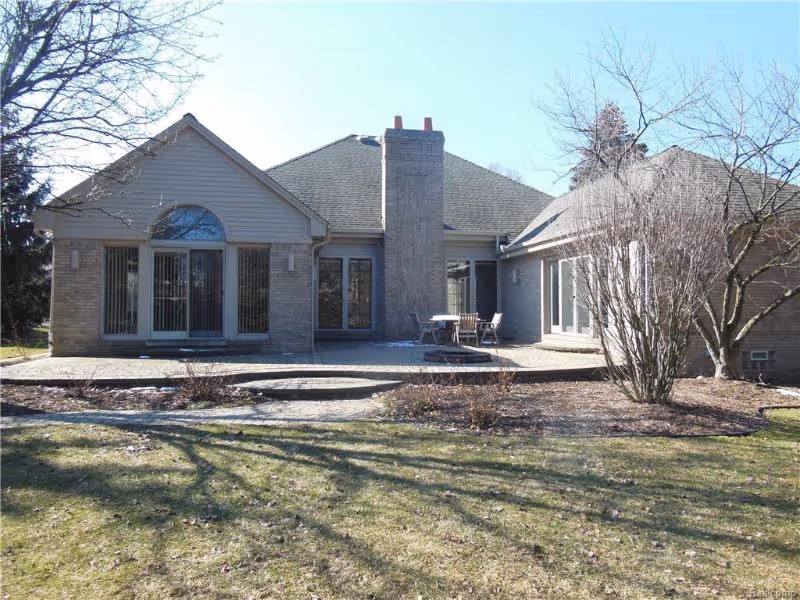 Exterior view of a single-story brick building with large windows and a central chimney, surrounded by a lawn and leafless trees under a clear blue sky.