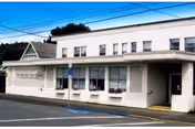 Exterior view of a single-story white building with multiple windows and a covered entrance. The building has a sign that reads 'Myrtle Care Center' and is situated next to a street with a handicapped parking space visible in front.