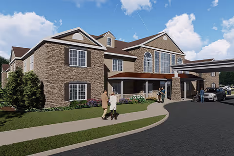 Exterior view of a senior living facility building with stone and beige siding, large windows, and a covered entrance. People are walking on the sidewalk and near the entrance, with a car parked under the covered area. The sky is blue with some clouds.