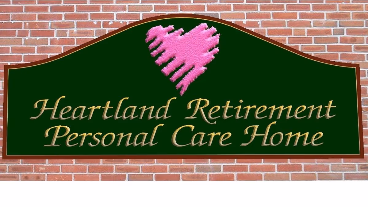 A green sign mounted on a brick wall with a pink heart graphic above the text that reads 'Heartland Retirement Personal Care Home'.